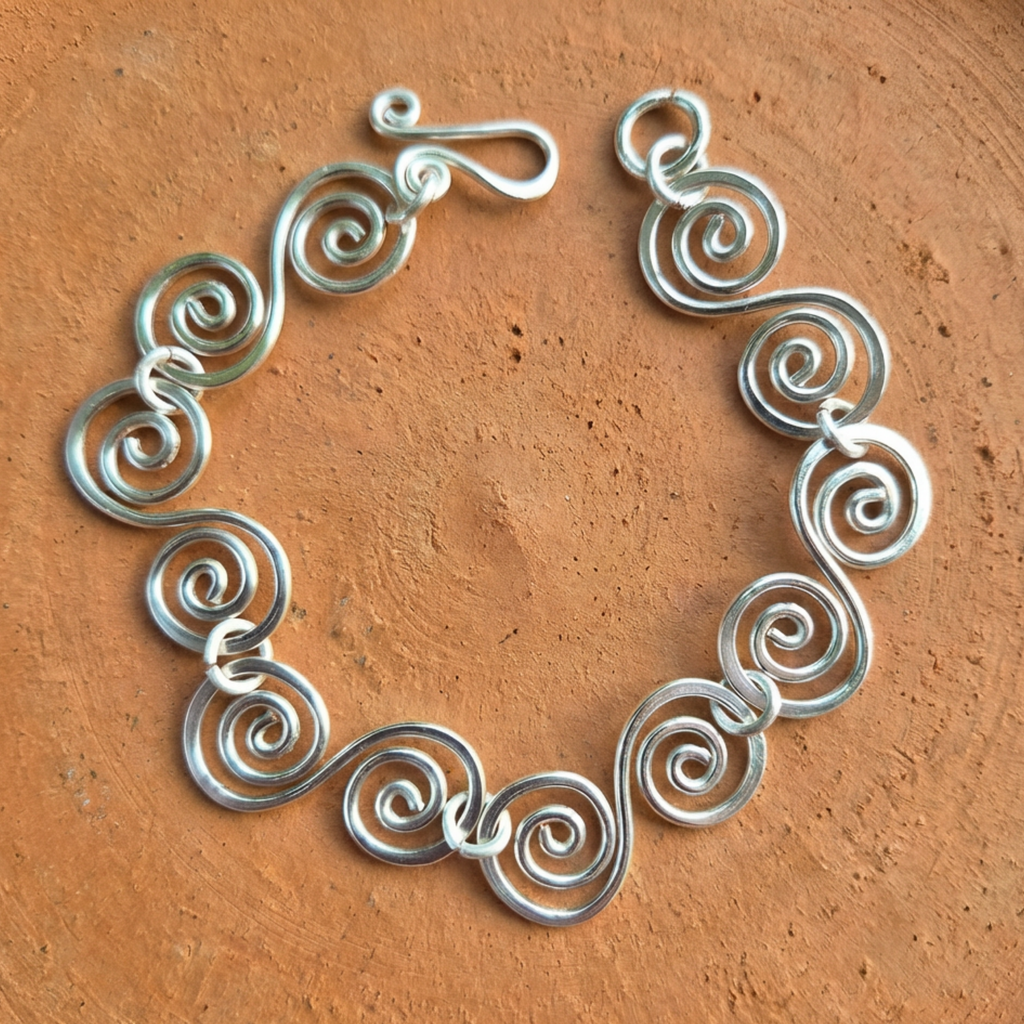 S shaped large spirals linked with jump rings bracelet with a simple fish hook clasp on a terracotta surface