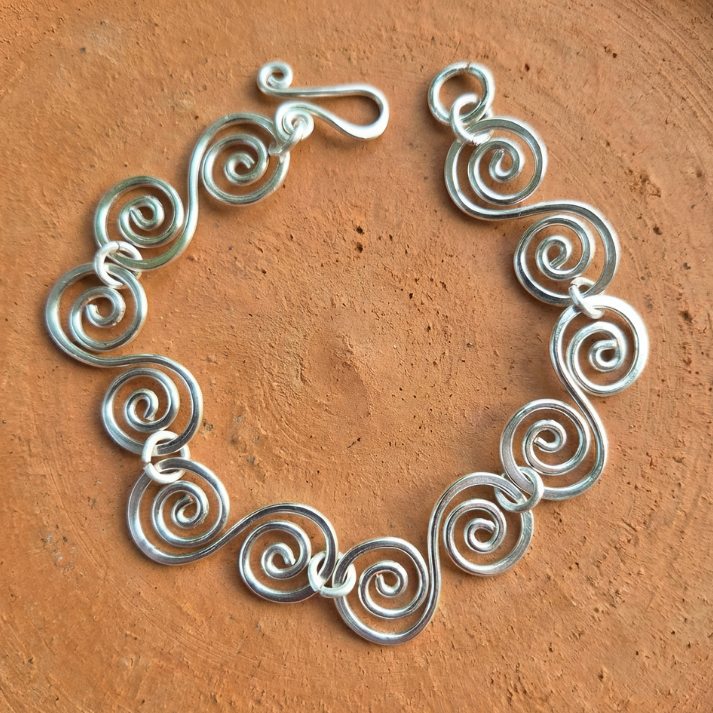 S shaped large spirals linked with jump rings bracelet with a simple fish hook clasp on a terracotta surface