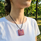 Person wearing a white shirt with a pink pendant necklace in a park setting