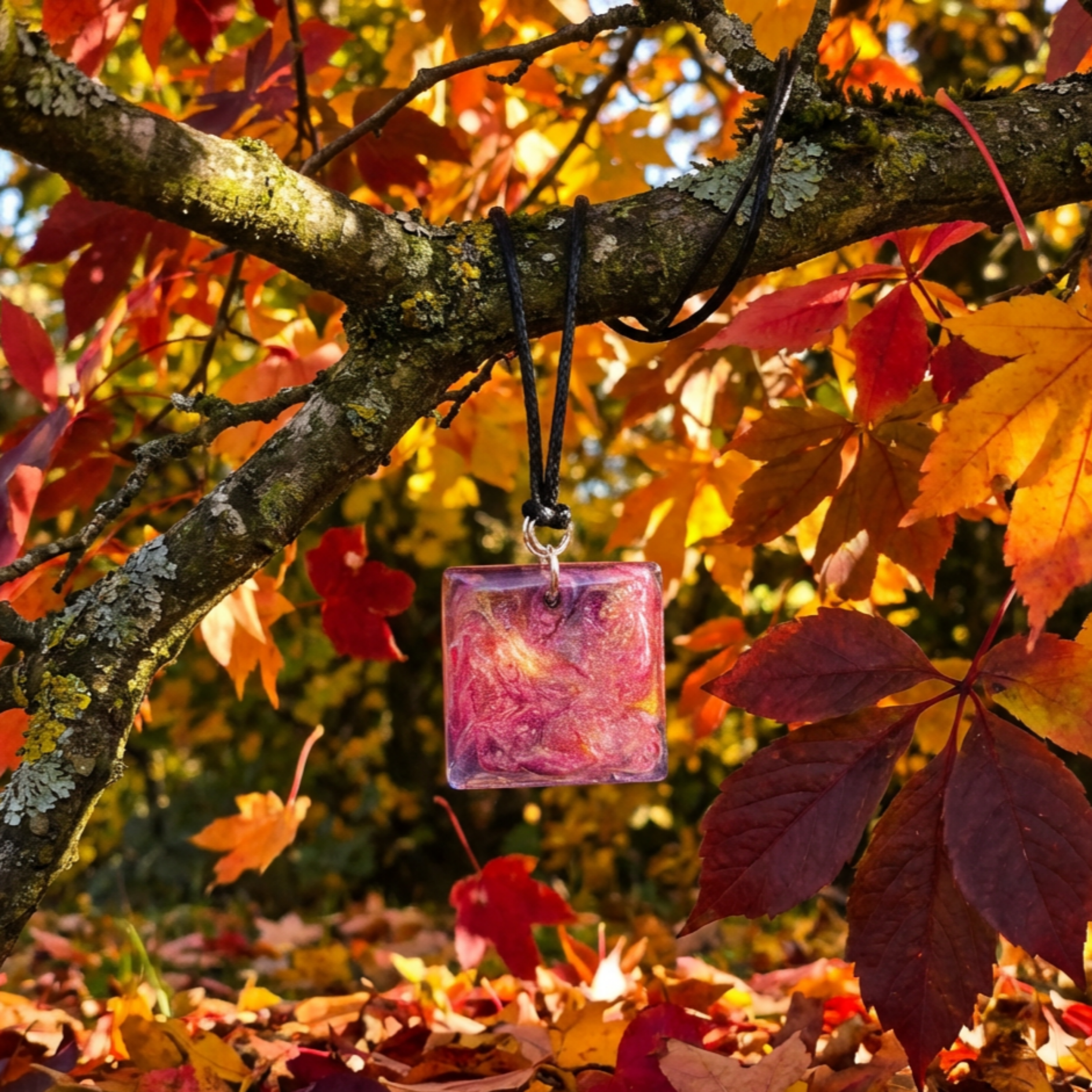 Pink square pendant hanging from a branch with autumn leaves