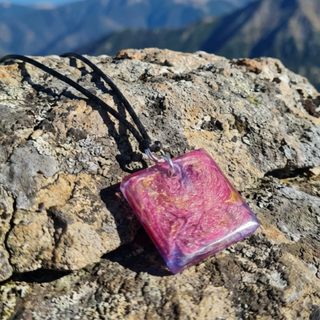 Distinctive square resin pendant with pink, purple and gold swirling pattern on a rock surface