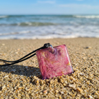 Square resin pendant with coloured swirls sitting in the sand