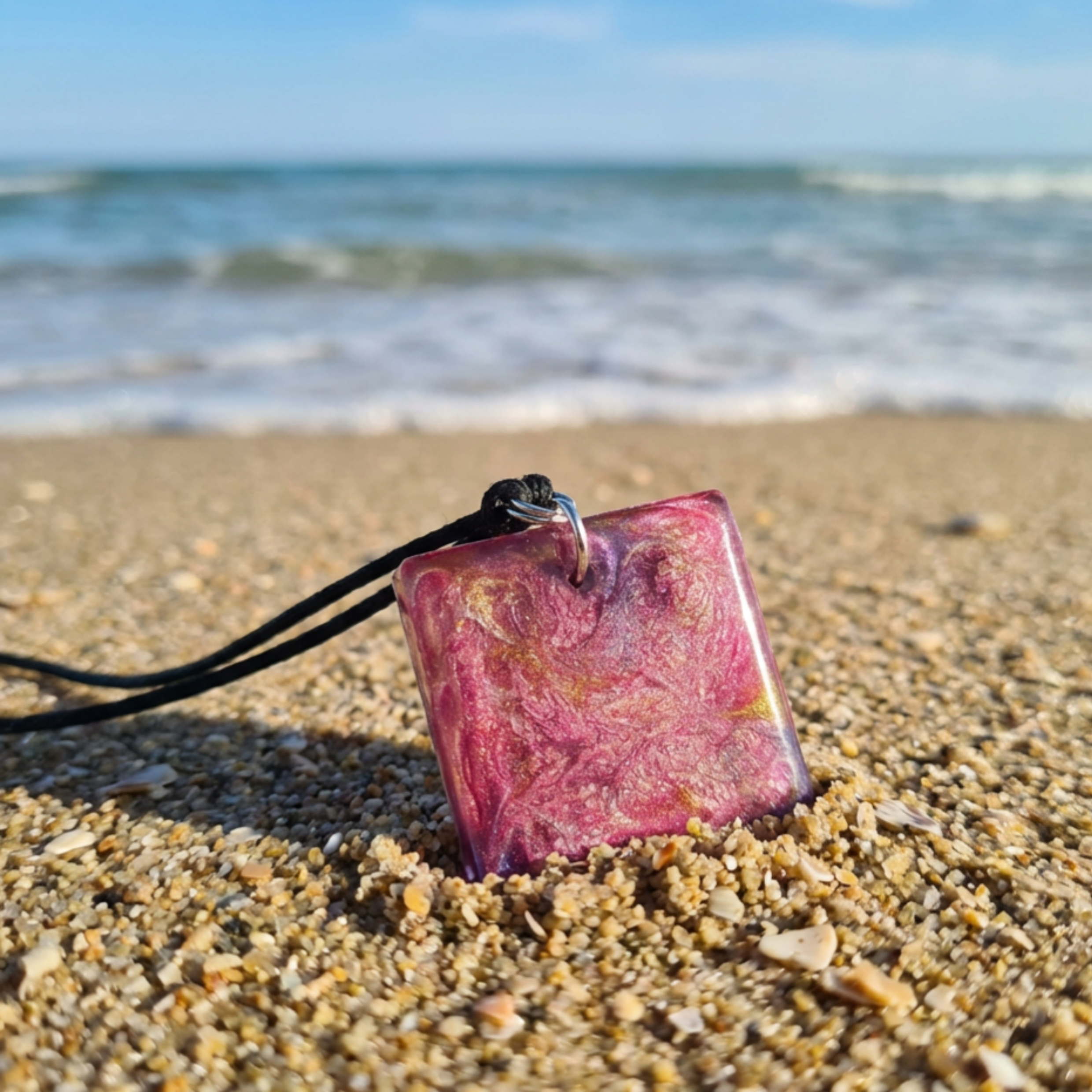 Square resin pendant with coloured swirls sitting in the sand