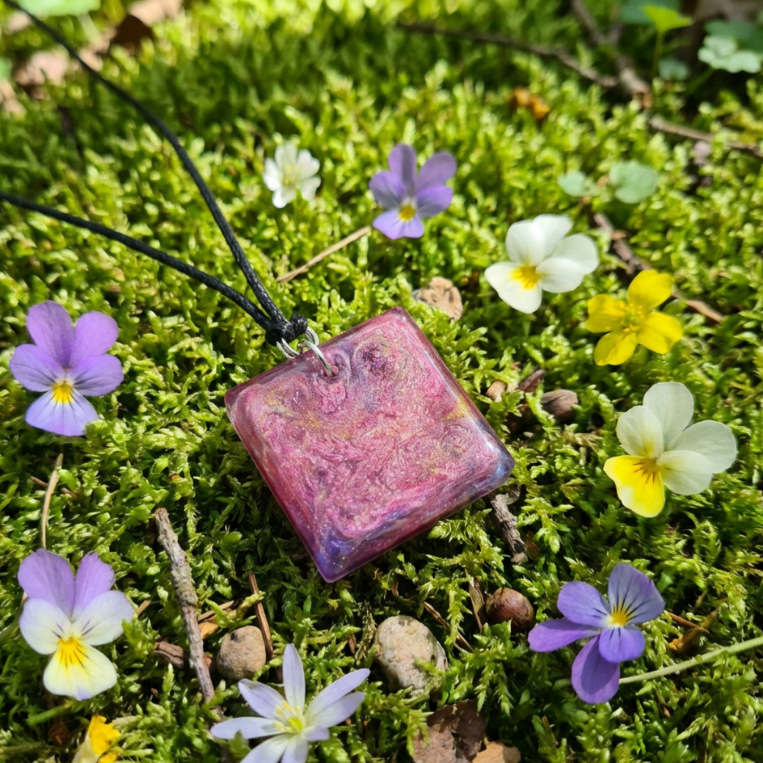 Pretty square pink purple gold pendant sitting on moss surrounded by flowers