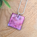 Pink square pendant necklace on a wooden surface