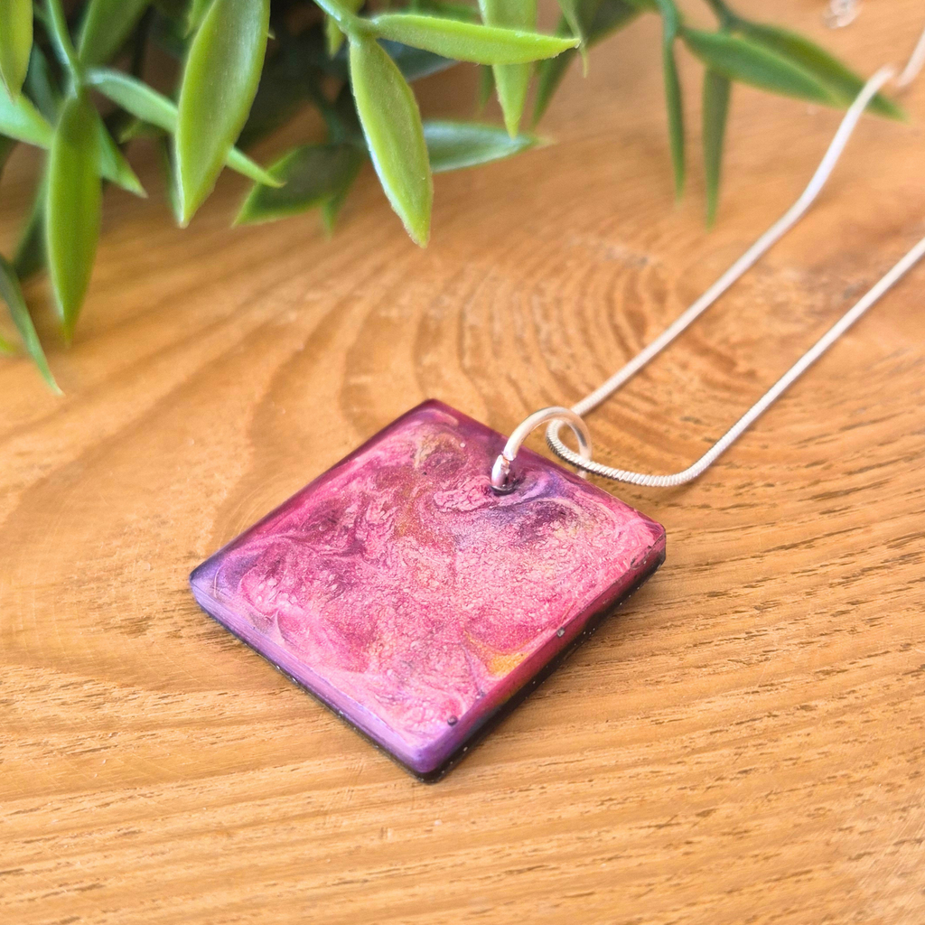 Square pink purple and gold pendant on a silver snake chain on a wooden surface