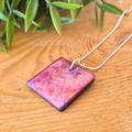 Square pink purple and gold pendant on a silver snake chain on a wooden surface