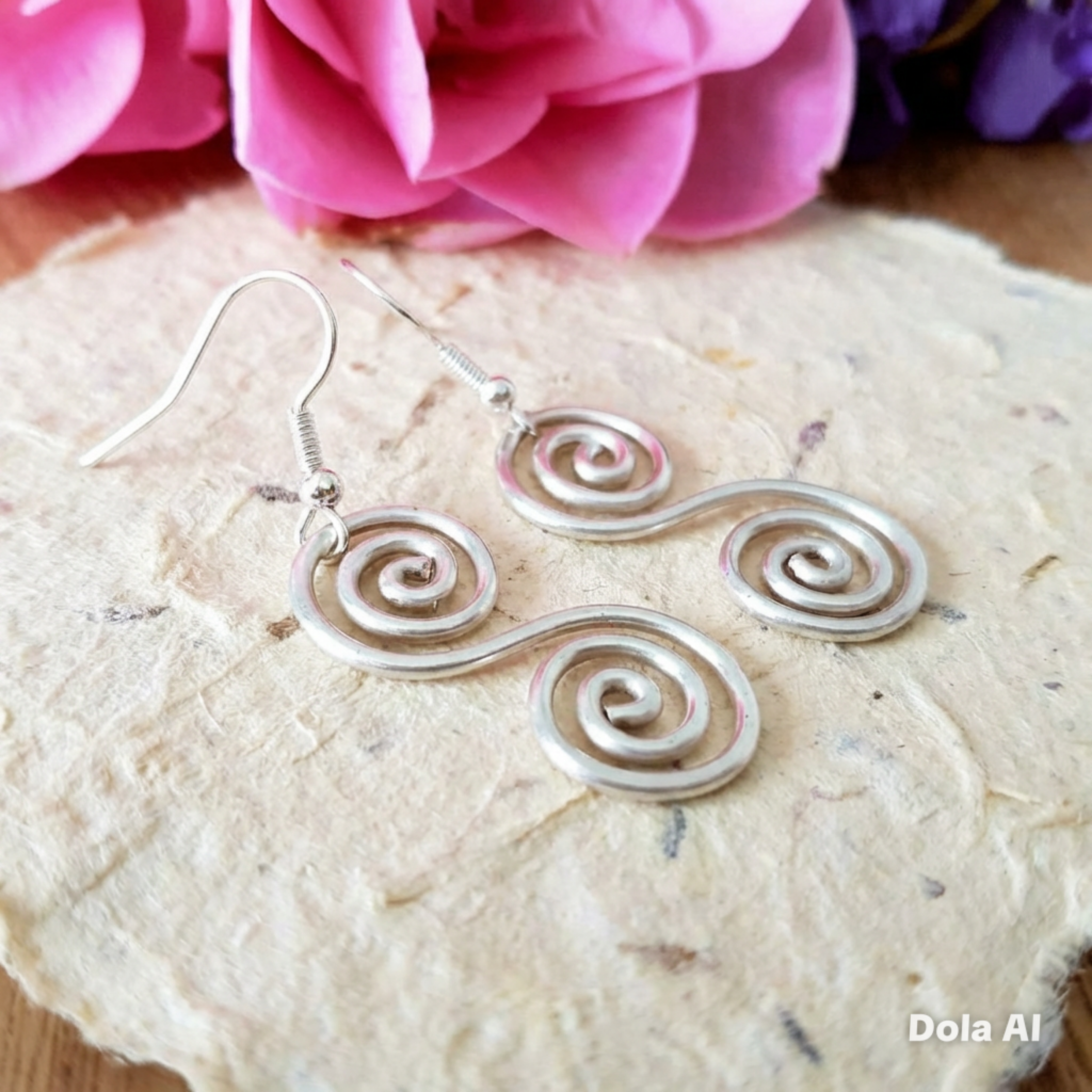 Silver spiral earrings on a stone surface with pink flowers in the background