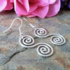 Silver spiral earrings on a stone surface with pink flowers in the background