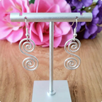 Silver spiral earrings on a stand with flowers in the background