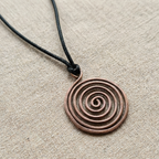Copper spiral pendant on a black cord against a beige fabric background