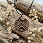 Copper spiral pendant on a black cord with dried flowers and wood