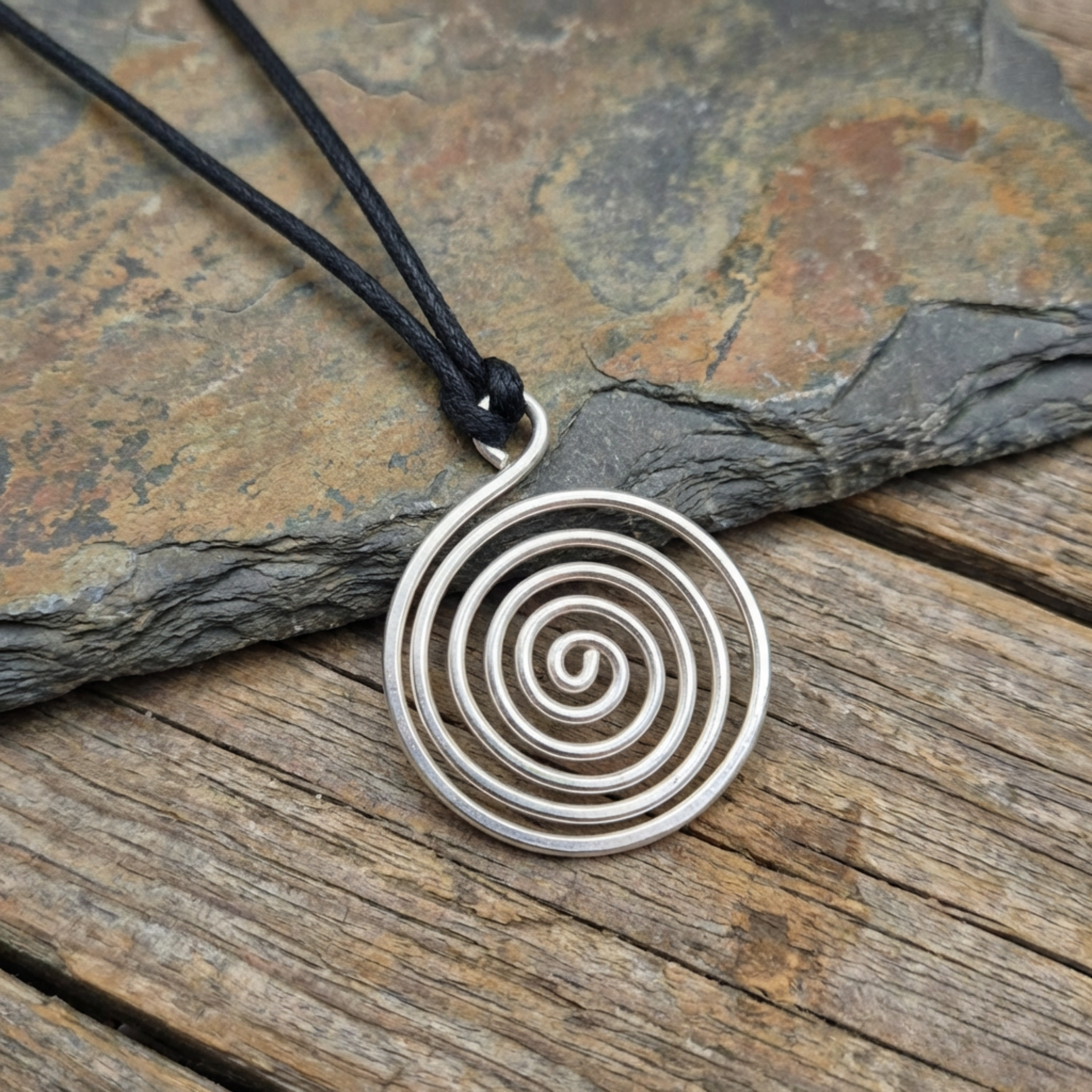 Silver spiral pendant on a black cord against a stone and wood background