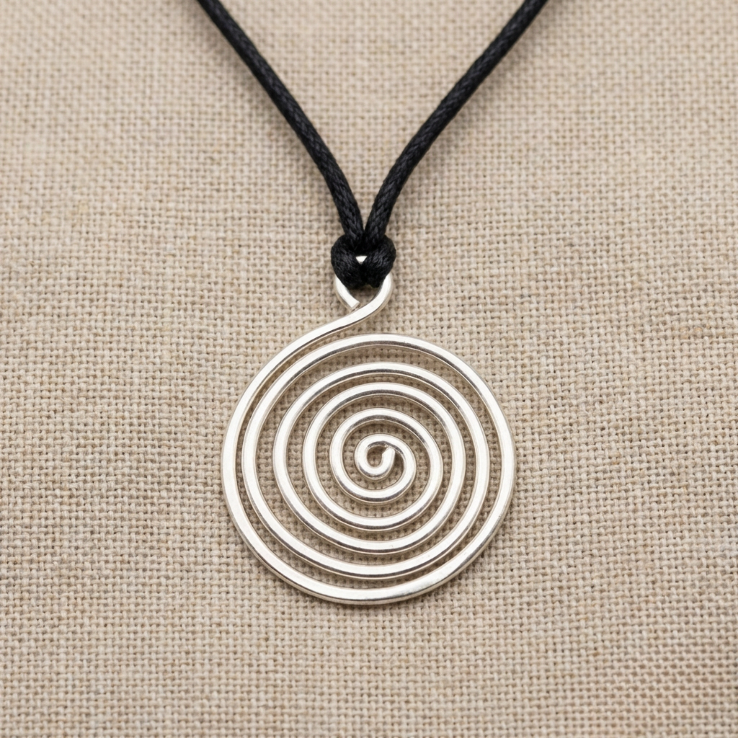 Silver spiral pendant on a black cord against a beige fabric background