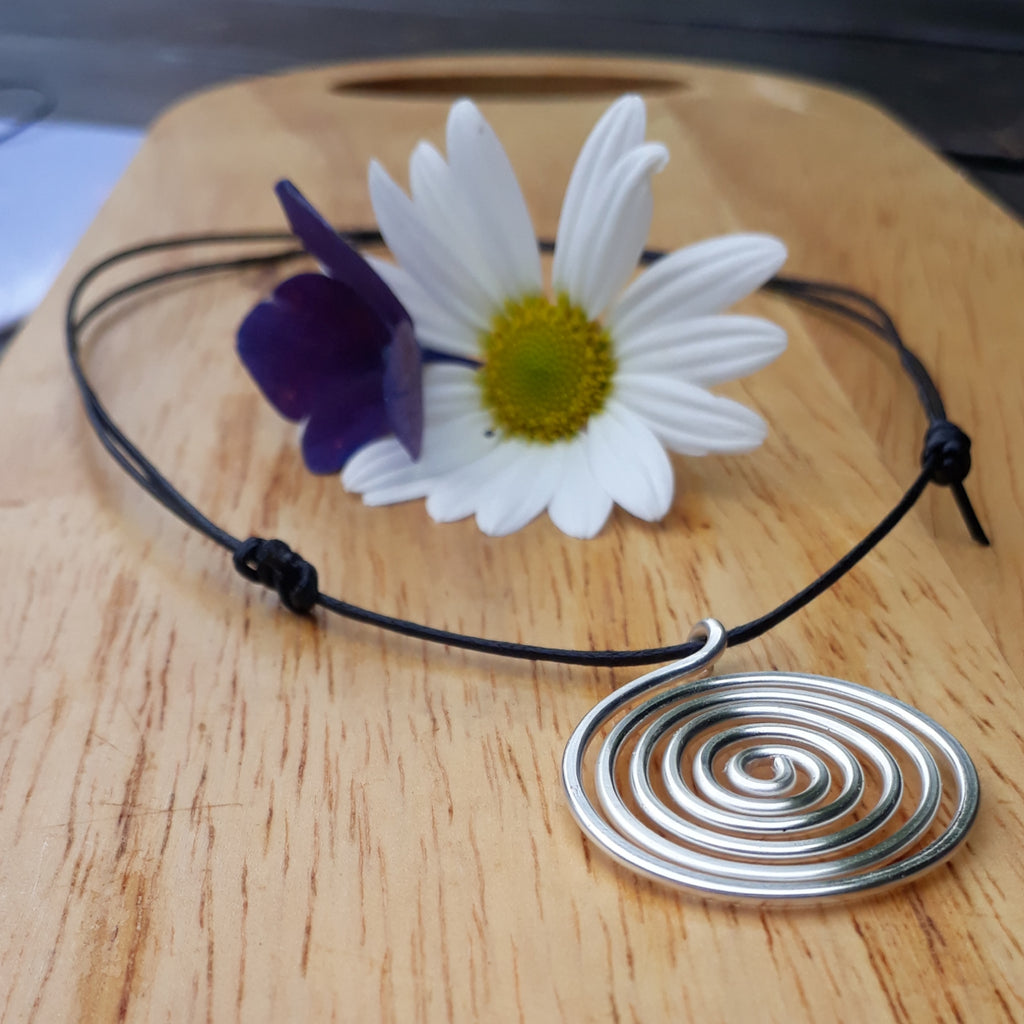 Necklace with a silver spiral pendant and decorative flowers on a wooden surface