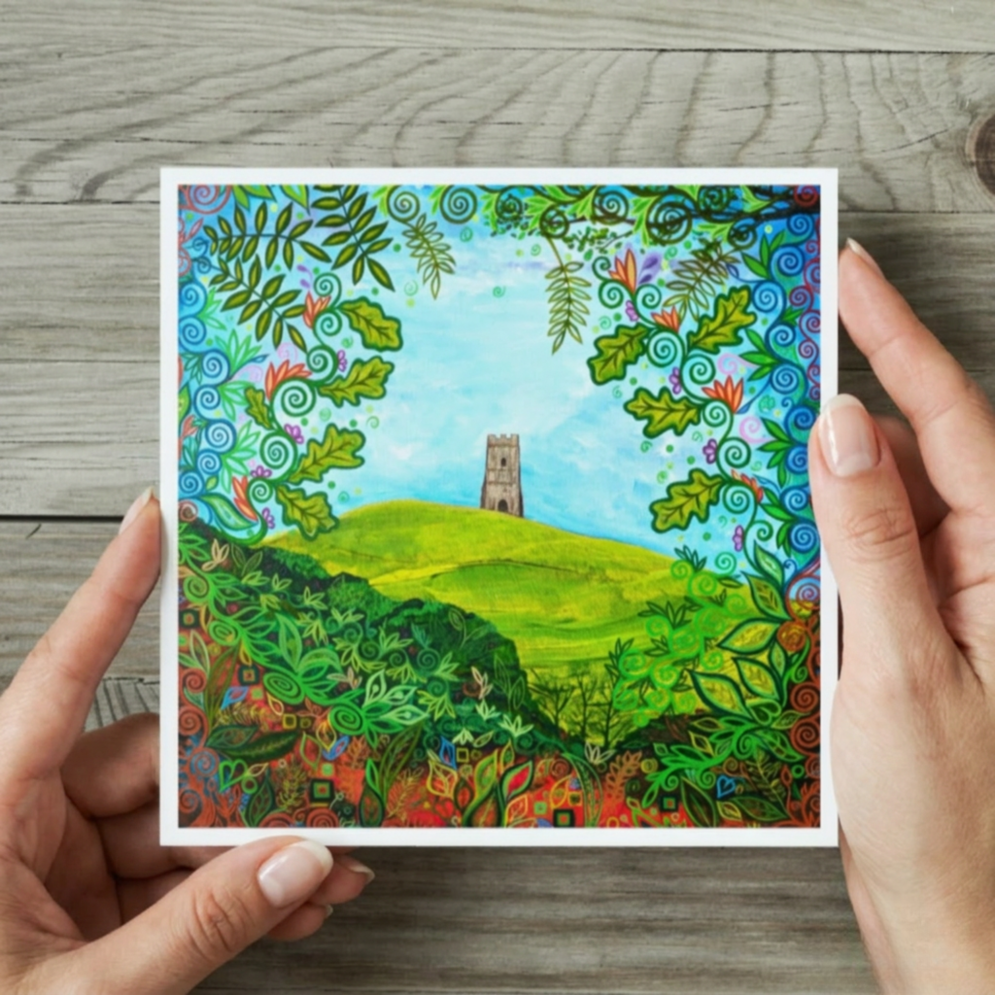 Colourful landscape painting held by hands on a wooden surface