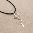 Silver spiral pendant on a black cord against a beige fabric background