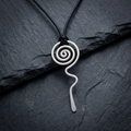 Silver spiral pendant on a black cord against a dark stone background