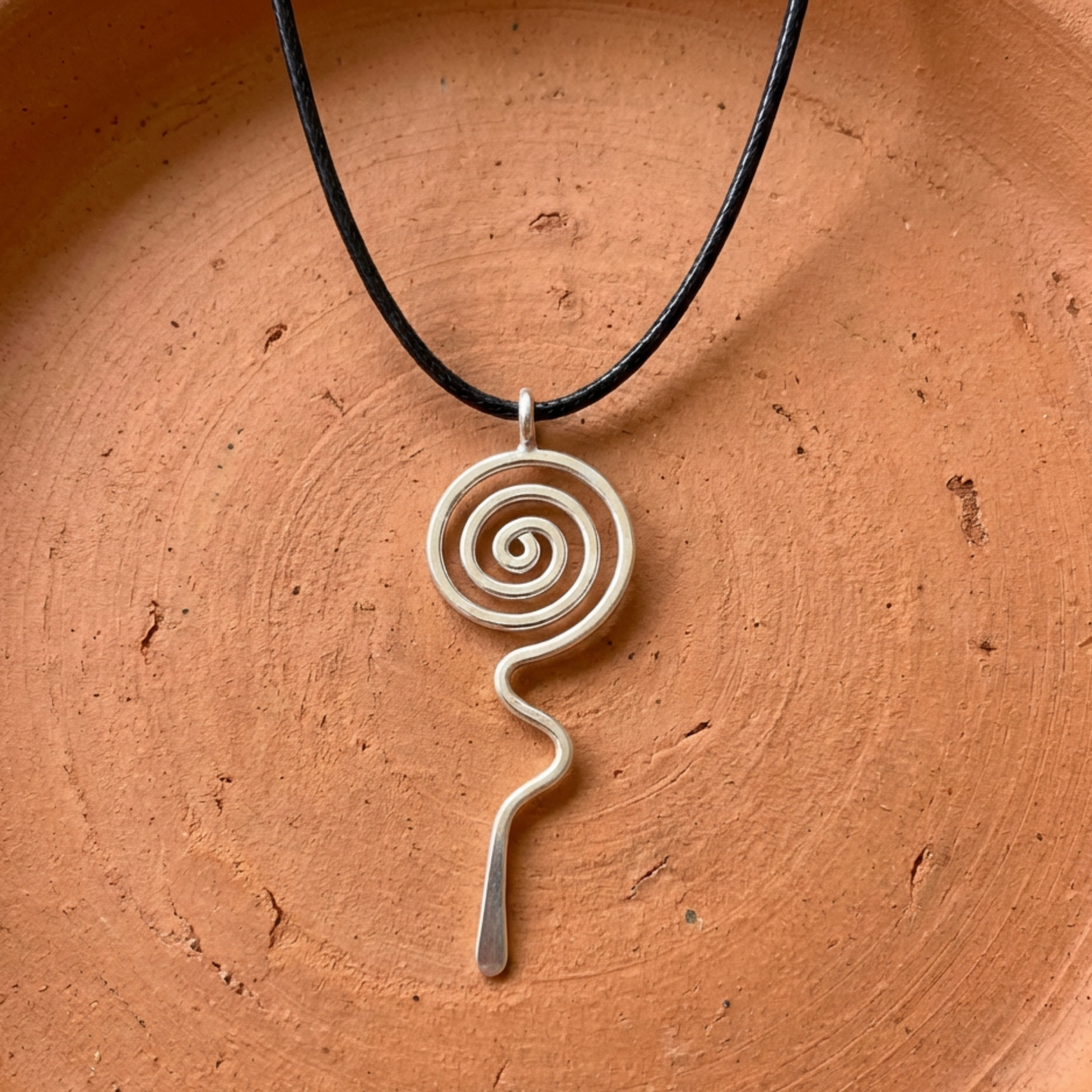Silver spiral pendant on a black cord against an orange-brown background