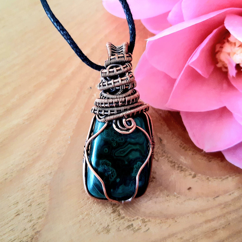 Necklace with a Malachite stone pendant on a wooden surface with a pink flower.