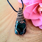 Necklace with a Malachite stone pendant on a wooden surface with a pink flower.