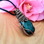 Necklace with a blue pendant on a wooden surface with pink flowers in the background
