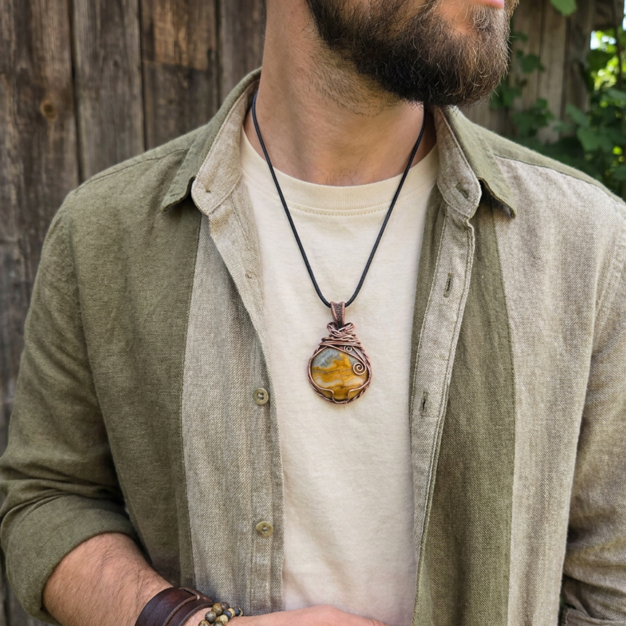 Man wearing a yellow picture jasper cabochon wrapped in copper wire pendant necklace outdoors