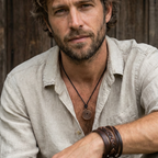 Man wearing a light-colored shirt with a copper spiral pendant necklace  sitting against a wooden background.