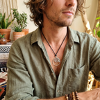Man wearing a green shirt with a necklace featuring a spiral fossil pendant, surrounded by plants.