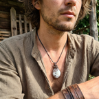 Man wearing a necklace with a white and copper pendant outdoors