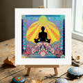 Colourful artwork of a meditating figure on a wooden easel with decorative stones and leaves.