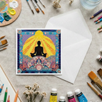 Colourful card with a meditating figure surrounded by mandala designs on a table with art supplies.