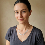 Woman wearing a gray shirt and spiral and chain necklace against a beige background