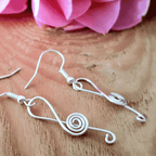 Silver wire earrings on a wooden surface with pink flowers in the background