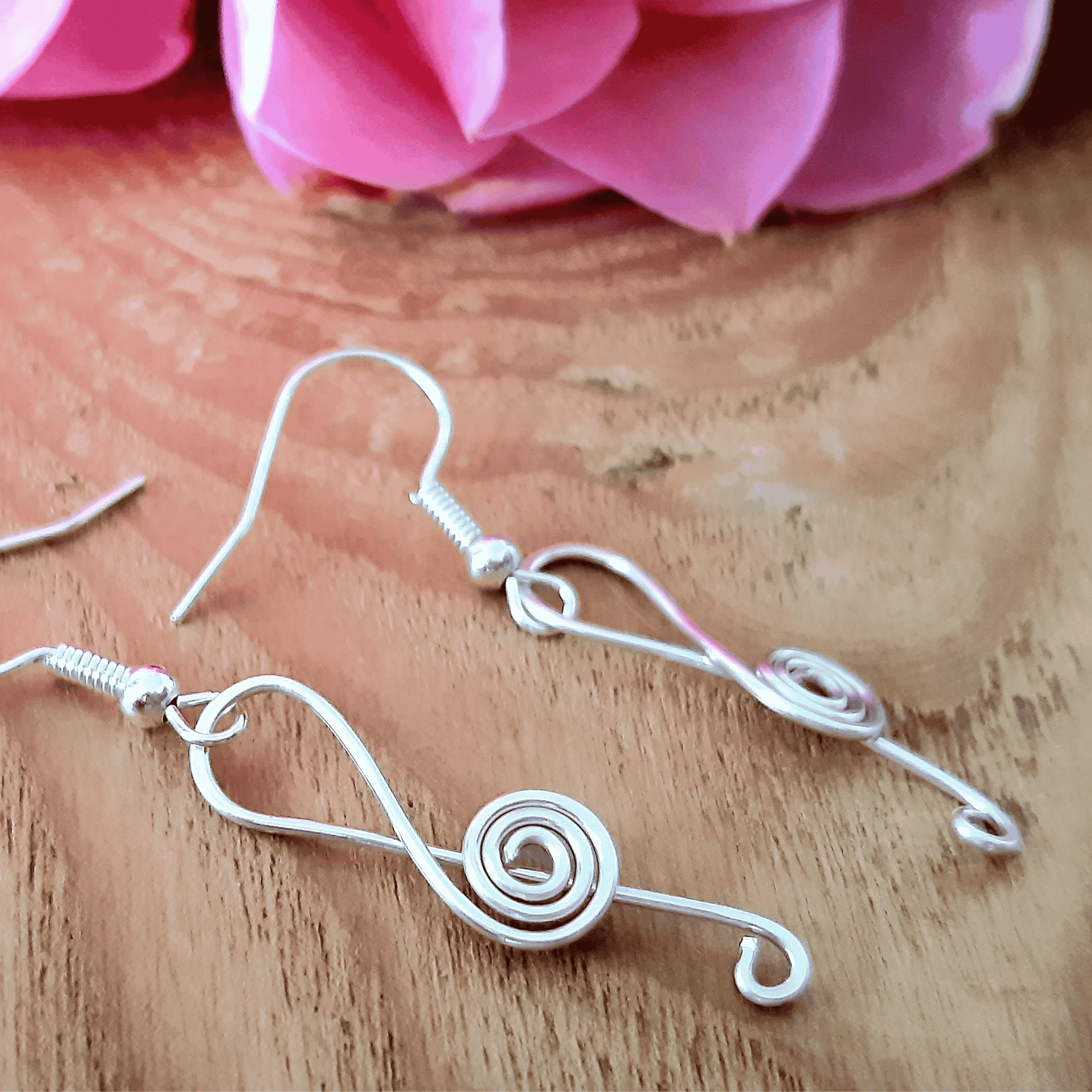 Silver wire earrings on a wooden surface with pink flowers in the background