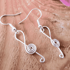 Silver wire music note earrings on a wooden surface