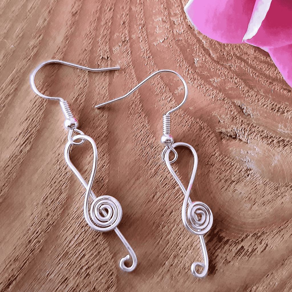 Silver wire-wrapped earrings on a wooden surface with pink fabric in the corner.