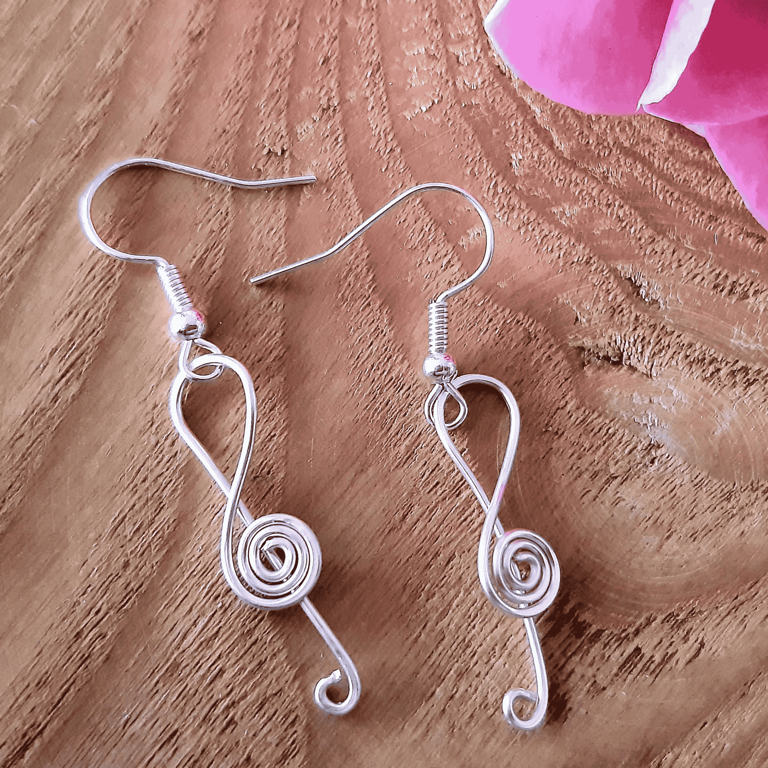 Silver wire-wrapped earrings on a wooden surface with pink fabric in the corner.