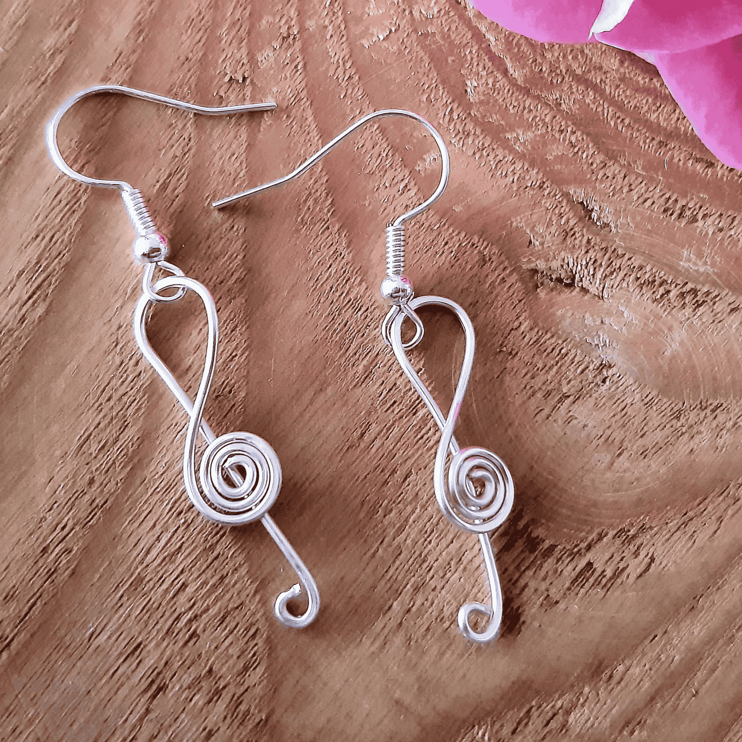 Silver wire-wrapped music earrings on a wooden surface with pink flowers.