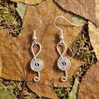 Silver treble clef-shaped earrings on a leafy background
