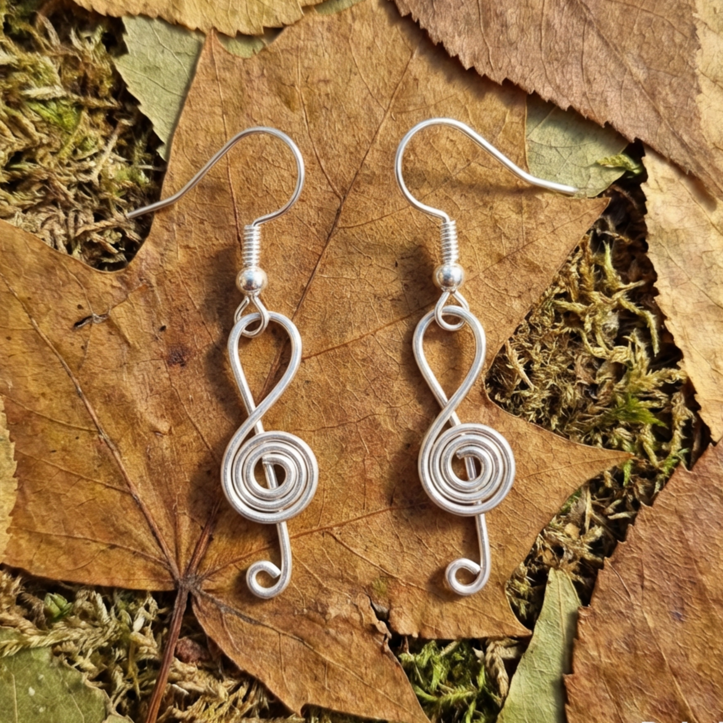 Silver treble clef-shaped earrings on a leafy background