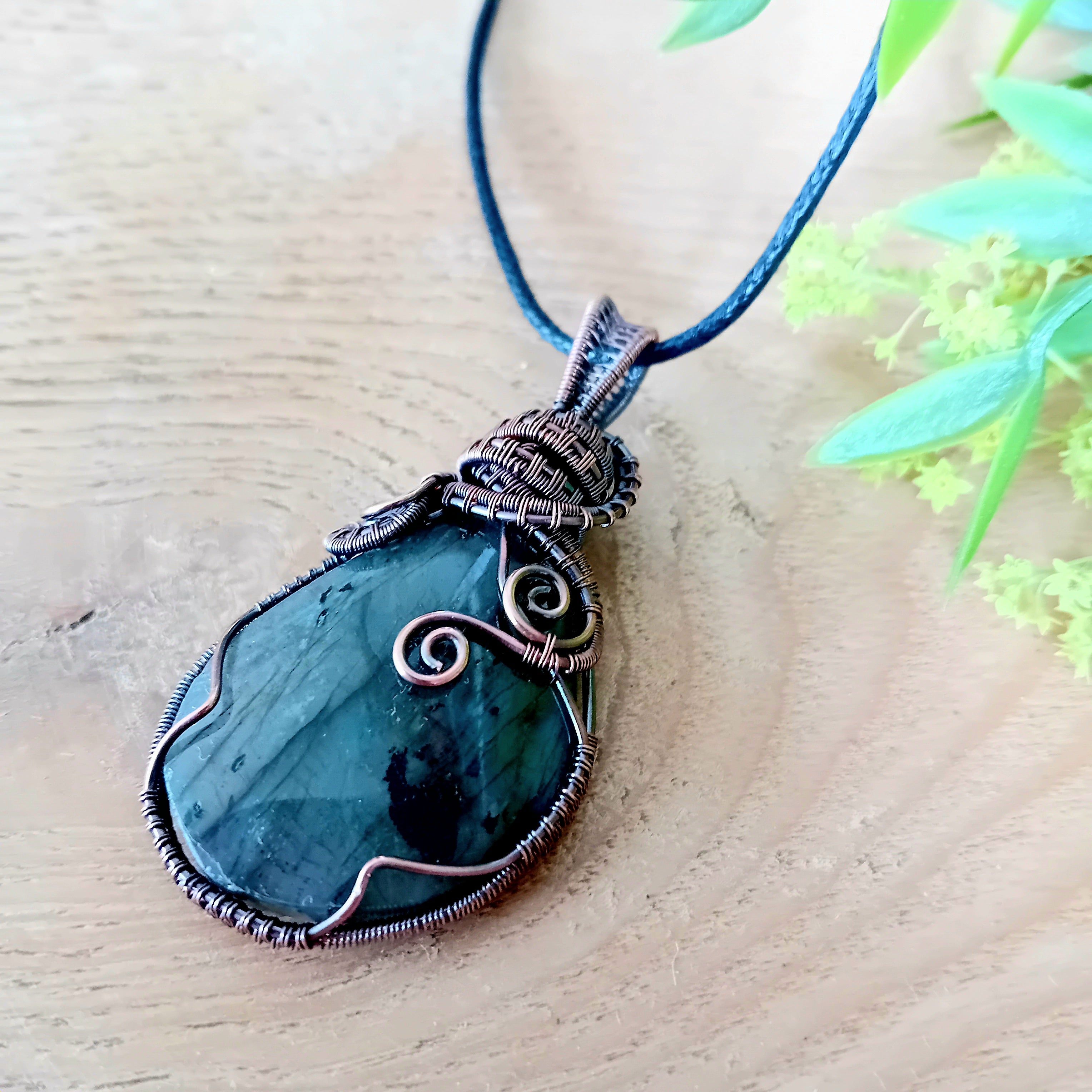Teal pendant with wire wrapping on a blue cord against a wooden background