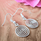 Silver spiral earrings on a wooden surface with a pink flower in the background