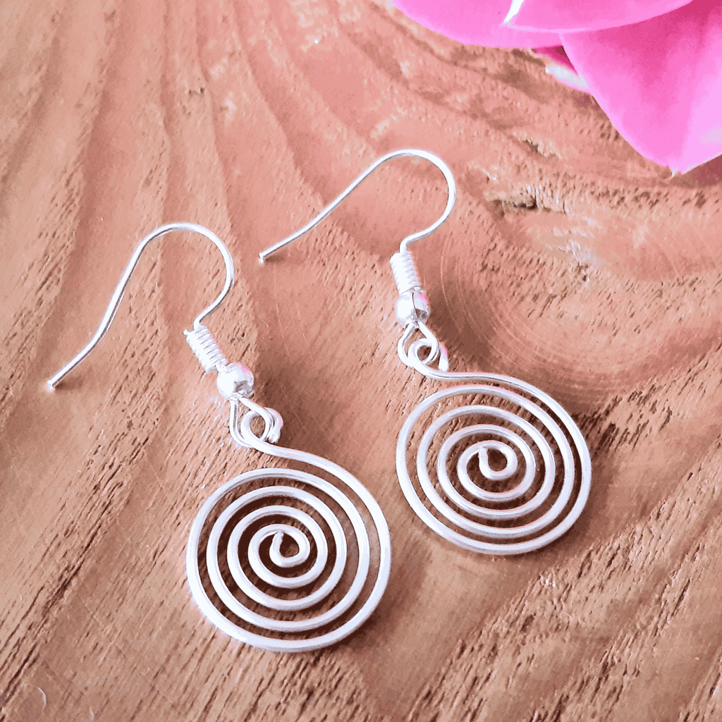 Silver spiral earrings on a wooden surface with pink flowers in the background