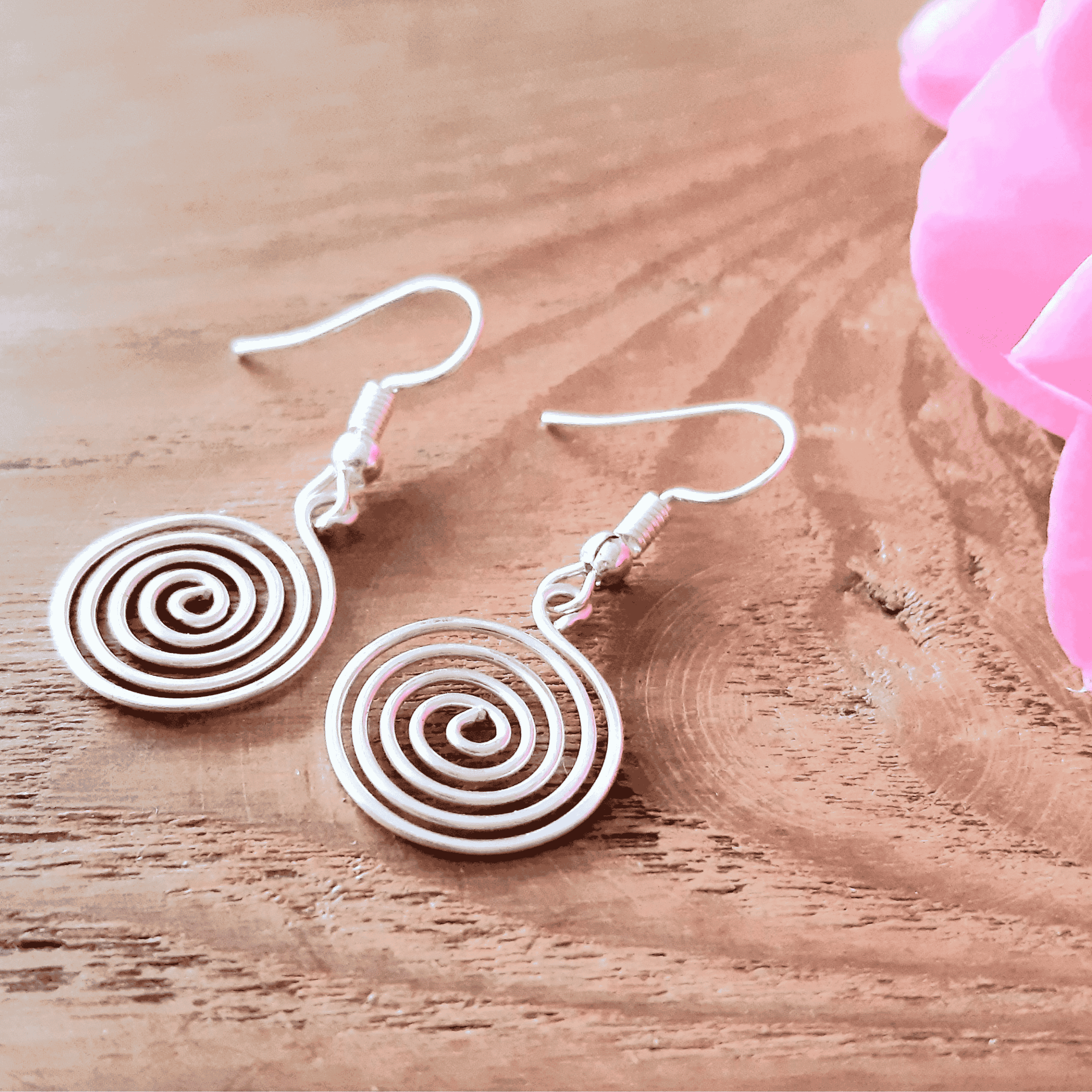Spiral earrings on a wooden surface with pink fabric in the background