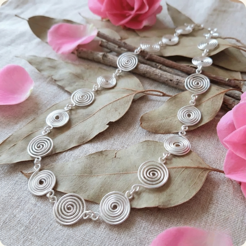 Silver spiral necklace on a leafy background with pink flowers