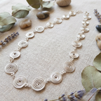 Silver spiral necklace on a textured surface with stones and lavender flowers