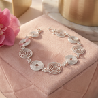 Silver spiral bracelet on a pink cushion with a pink flower and gold object in the background