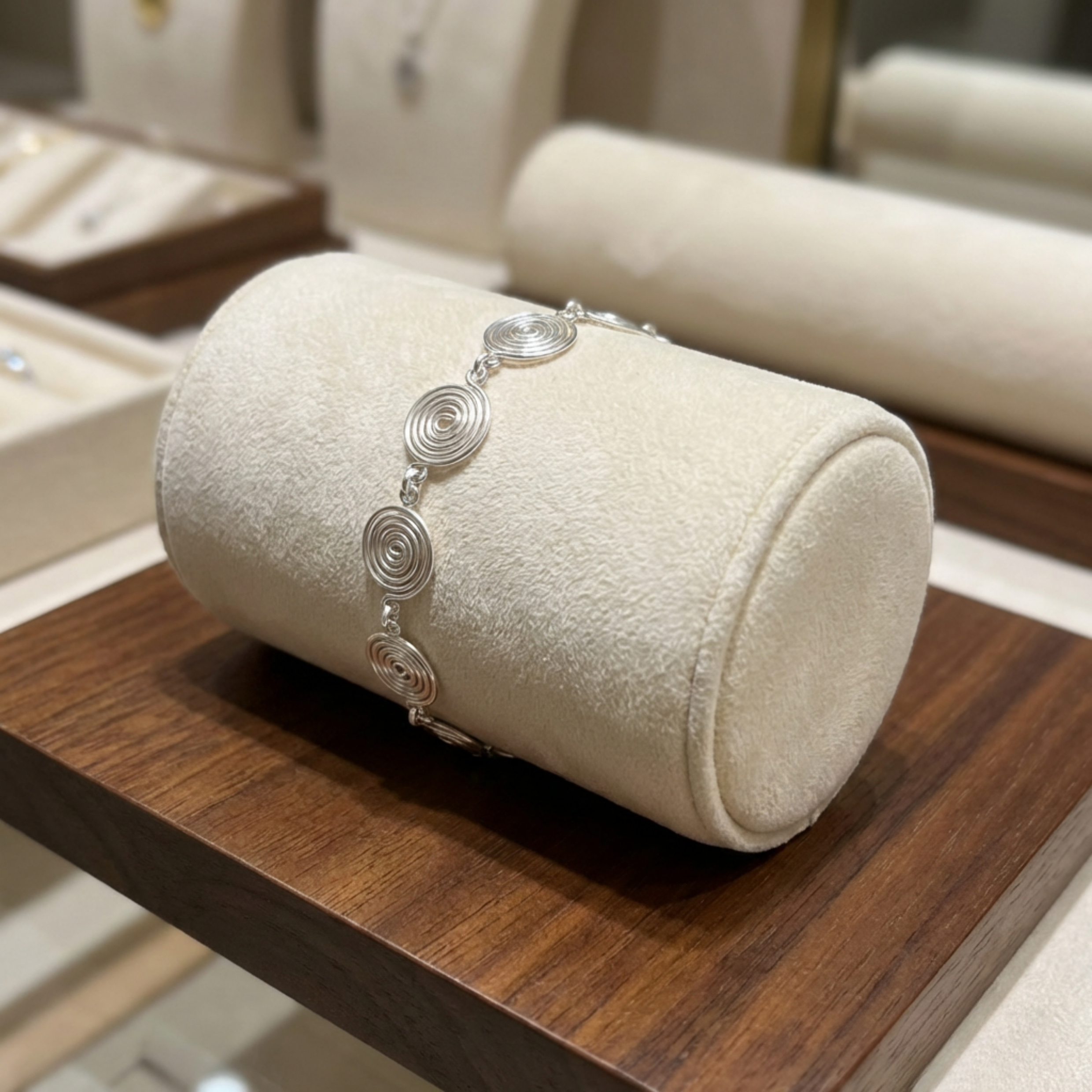Silver bracelet on a cylindrical jewellery display stand with a wooden surface.