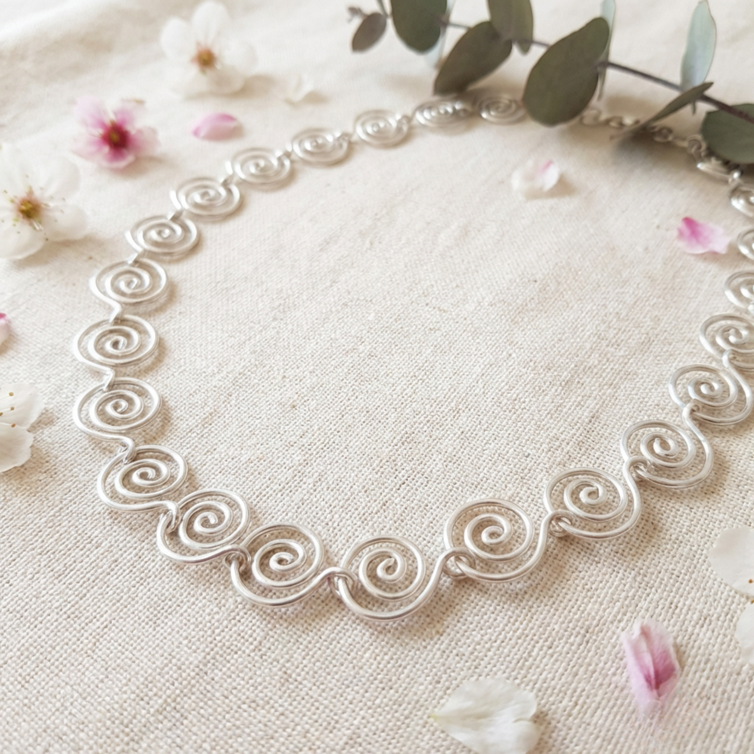 Silver necklace with intricate design on a light fabric background with flowers